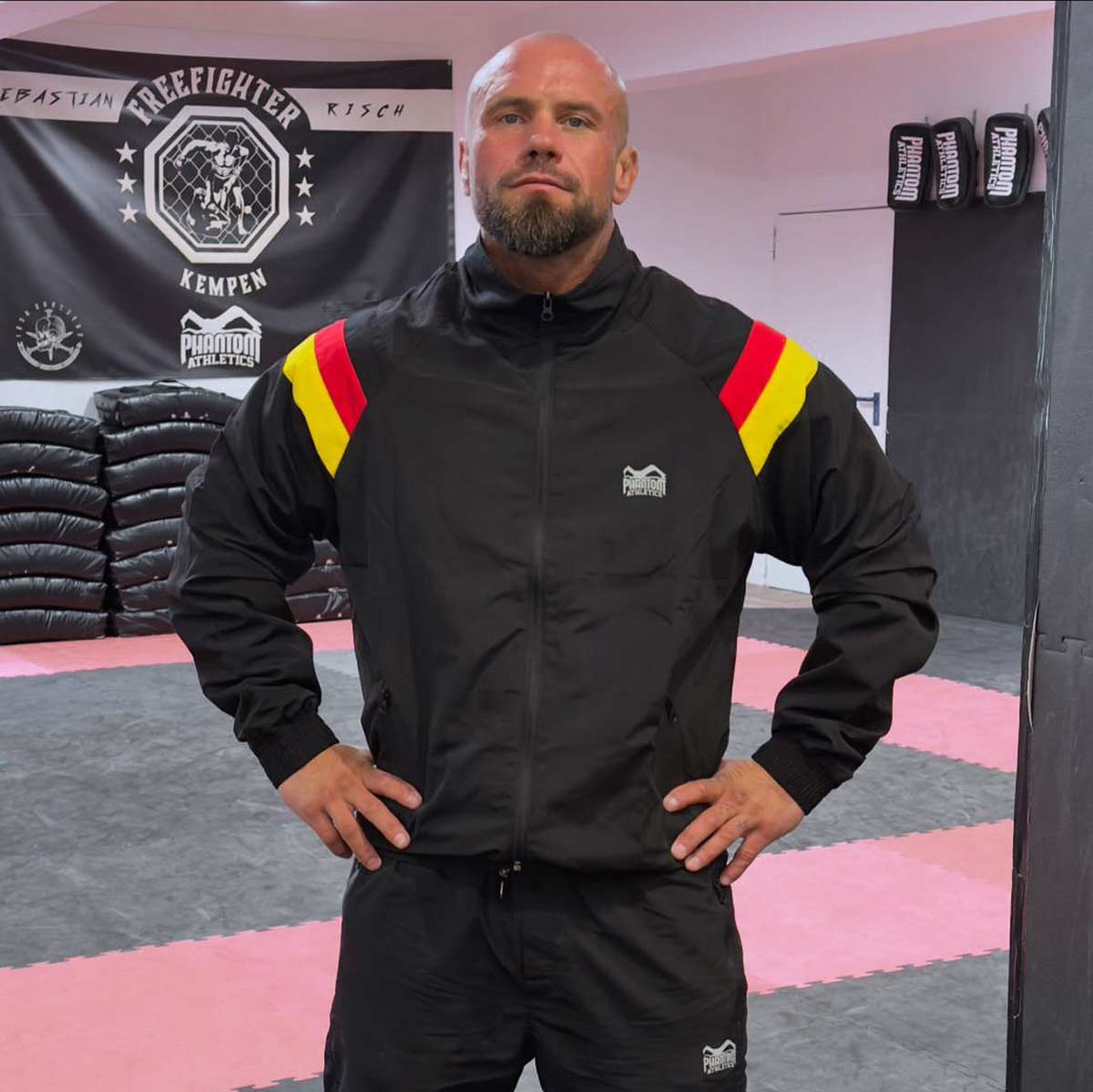 Der DMC Team Germany Trainingsanzug von Phantom Athletics bietet hohen Tragekomfort und Funktionalität für Kampfsport und Fitness. Das leichte, atmungsaktive Material und das sportliche Design in den Farben Schwarz, Rot und Gelb machen ihn ideal für Training und Freizeit.