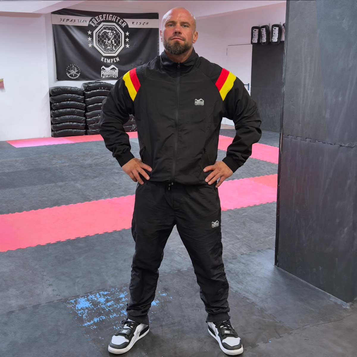 MMA Pro Fighter Sebastian Risch mit dem Phantom DMC Kampfsport Trainingsanzug. Der DMC Team Germany Trainingsanzug von Phantom Athletics bietet hohen Tragekomfort und Funktionalität für Kampfsport und Fitness. Das leichte, atmungsaktive Material und das sportliche Design in den Farben Schwarz, Rot und Gelb machen ihn ideal für Training und Freizeit.